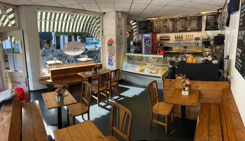 Het interieur van Pico-Bello met houten tafels, banken en de toonbank met menuborden